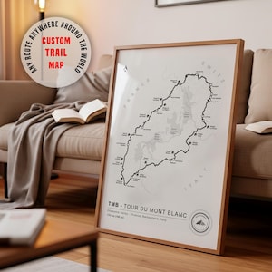 May include: A framed map print titled TMB - TOUR DU MONT BLANC, featuring a black line route through France, Switzerland, and Italy. The white map displays mountain peaks, locations, and the text 170 km (106 mi). A circular badge in the corner reads ANY ROUTE ANYWHERE AROUND THE WORLD CUSTOM TRAIL MAP.