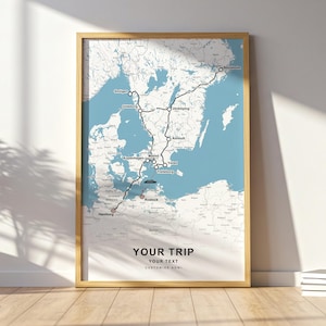 May include: A framed map print with a light blue background and a route marked in black, connecting cities like Stockholm, Hamburg, and Copenhagen. The text "YOUR TRIP" is at the bottom, with space for customization.