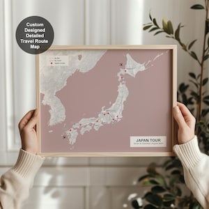 Könnte beinhalten: Eine gerahmte Karte von Japan mit einem staubrosa Hintergrund und einem hellen Holzrahmen. Die Karte zeigt eine Reiseroute mit roten Punkten und Flugzeugsymbolen. Der Text auf der Karte lautet "Japan Tour" und "Custom Designed Detailed Travel Route Map."