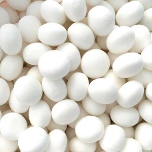 May include: A close-up of a collection of white, oval sweets. The sweets are smooth and have a matte finish. They are packed closely together, filling the frame. The overall impression is of a uniform texture and colour.