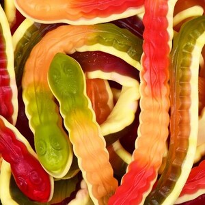 May include: A close-up shot of a pile of gummy worm sweets. The sweets are in various colours, including red, orange, yellow, and green. The gummy worms are a popular confectionery item.