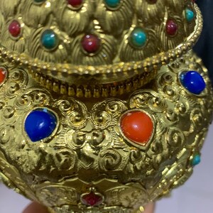 May include: Ornate gold-colored vessel with intricate scrollwork and embedded gemstones. The vessel features red, blue, and turquoise stones, adding vibrant color to the design. The overall aesthetic suggests a focus on decorative arts and craftsmanship.