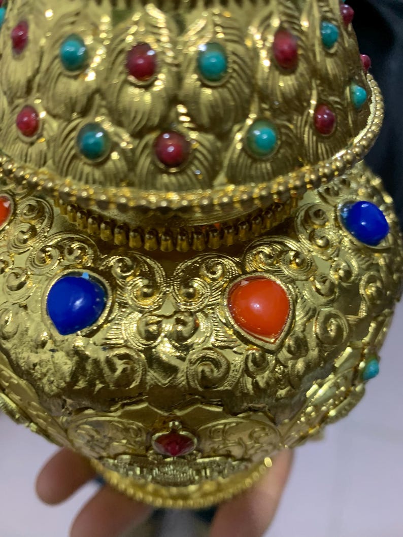 May include: Ornate gold-colored vessel with intricate scrollwork and embedded gemstones. The vessel features red, blue, and turquoise stones, adding vibrant color to the design. The overall aesthetic suggests a focus on decorative arts and craftsmanship.