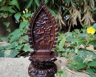 May include: A dark brown wooden stand featuring a vertical back panel carved with cloud and floral motifs, set upon a circular base with a lotus petal design. The piece has a flame-shaped top edge and a smooth, polished finish throughout.