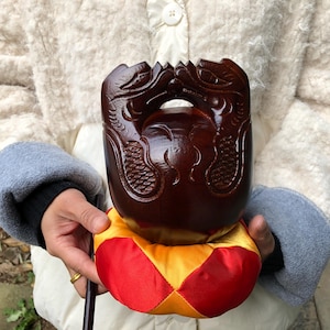 May include: A dark brown, carved wooden object featuring two dragon figures facing each other. The object rests on a red and yellow cushion. The dragons are intricately detailed, and the wood has a polished finish.