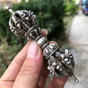 Puede incluir: Objeto ritual plateado ornamentado con intrincados diseños florales y geométricos. El objeto tiene una sección central bulbosa y termina en una punta. La detallada artesanía sugiere un propósito ceremonial o decorativo.