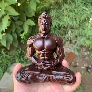 May include: A dark brown wooden Buddha statue in a seated meditation pose. The statue has a muscular physique and detailed carving, with a serene facial expression. The statue is approximately 6 inches tall.
