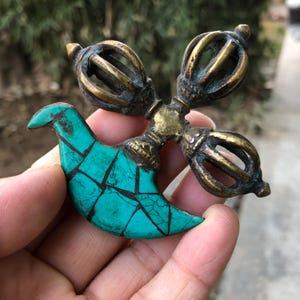 May include: An antique brass vajra, a ritual object, with a turquoise bird-shaped inlay. The vajra features intricate detailing and a weathered appearance, suggesting age. The turquoise inlay is a vibrant contrast to the brass.