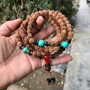 May include: A brown mala bead necklace with turquoise and red beads. The necklace is made of 108 beads and has a tassel.