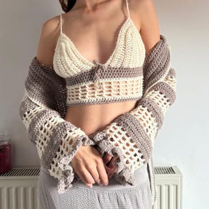 May include: A cream and brown crochet top with spaghetti straps and a matching open-front cardigan. The top features a triangle-shaped bust and a decorative tie. The cardigan has bell sleeves with a scalloped edge. The outfit is handmade.