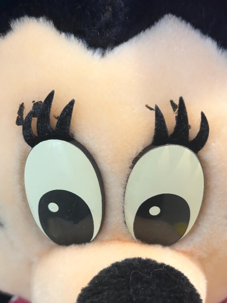 May include: Close-up of a plush toy's face. The toy has large, black eyes with white pupils and black eyelashes. The face is pink and fuzzy.