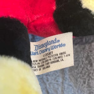 May include: A red, black, and yellow plush toy with a Disneyland Walt Disney World tag. The tag reads "&copy;DISNEY NEW MATERIALS POLYESTER FIBERS 525:PA 1379:OHIO PA 1378:MASS T-616 MASA TRADING CORP. BURBANK, CA, UCT OF SRILANKA"