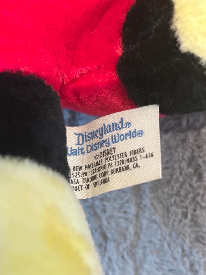 May include: A red, black, and yellow plush toy with a Disneyland Walt Disney World tag. The tag reads "&copy;DISNEY NEW MATERIALS POLYESTER FIBERS 525:PA 1379:OHIO PA 1378:MASS T-616 MASA TRADING CORP. BURBANK, CA, UCT OF SRILANKA"