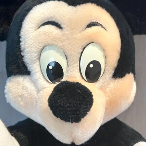 May include: A plush Mickey Mouse toy with black ears, a black nose, and large white eyes. The toy is made of soft, fuzzy fabric.