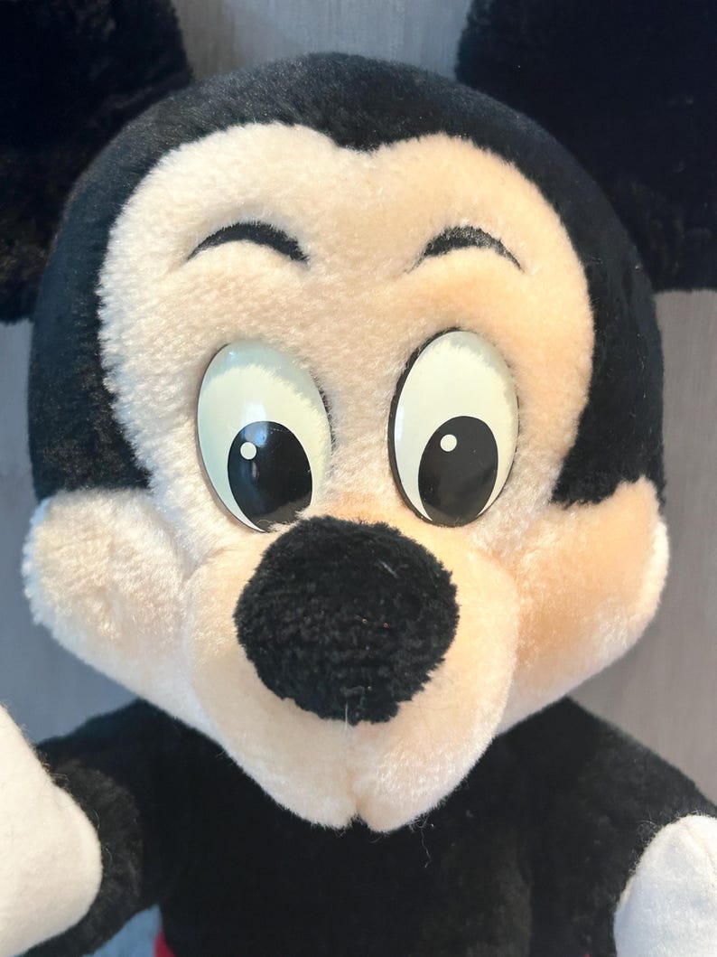 May include: A plush Mickey Mouse toy with black ears, a black nose, and large white eyes. The toy is made of soft, fuzzy fabric.