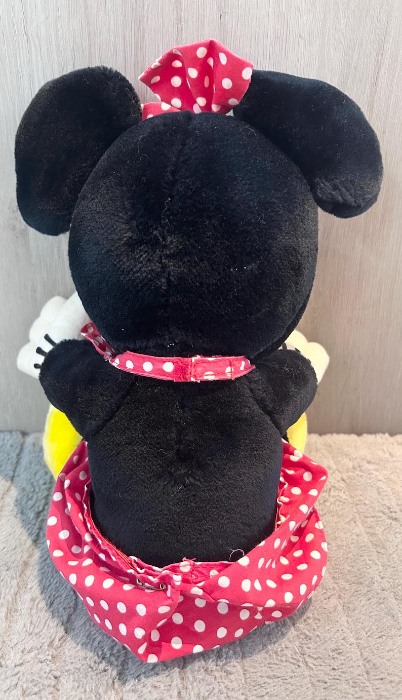 May include: A black and white plush toy of Minnie Mouse wearing a red dress with white polka dots and a red bow with white polka dots.