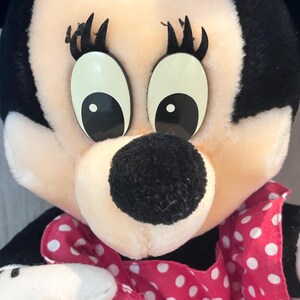 May include: A plush toy of a cartoon mouse wearing a pink dress with white polka dots. The mouse has large black eyes and a black nose.