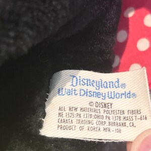 May include: A black and red plush toy with a white polka dot bow. The tag reads "Disneyland Walt Disney World" and "All new materials polyester fibers ME 1525:PA 1378:OHIO PA 1378:MASS T-616 CAMASA TRADING CORP. BURBANK, CA, PRODUCT OF KOREA MFR-100".