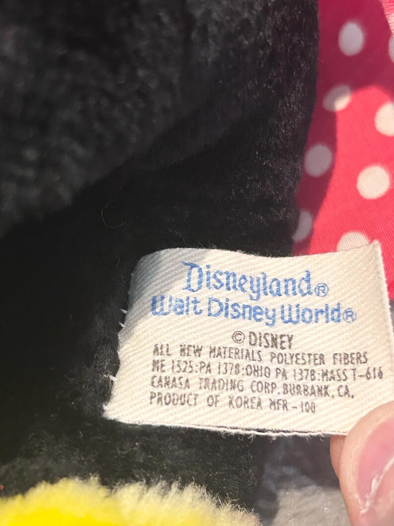 May include: A black and red plush toy with a white polka dot bow. The tag reads "Disneyland Walt Disney World" and "All new materials polyester fibers ME 1525:PA 1378:OHIO PA 1378:MASS T-616 CAMASA TRADING CORP. BURBANK, CA, PRODUCT OF KOREA MFR-100".