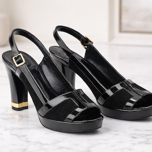 May include: Pair of black slingback platform sandals with high block heels. The sandals feature a glossy patent leather finish on the straps and toe box, with a suede panel and gold-tone hardware.