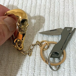 May include: A gold skull keychain with a small silver multi-tool attached to a gold key ring.