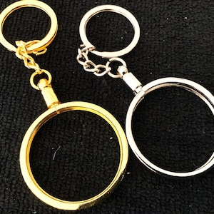 Op de afbeelding: Twee sleutelhangers, een gouden en een zilveren, met ronde ringen en een ketting. De gouden sleutelhanger heeft een grotere ronde ring met een kleinere ring eraan bevestigd. De zilveren sleutelhanger heeft een kleinere ronde ring met een grotere ronde ring eraan bevestigd.