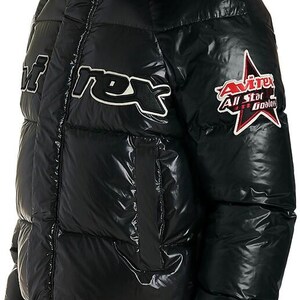 May include: Black puffer jacket with a glossy finish, featuring a hood with red lining. The jacket has white text and a star-shaped patch with text. A winter coat for cold weather.