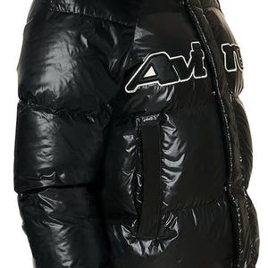 May include: Black puffer jacket with a glossy finish and a hood. The jacket features a red lining in the hood and a white and black logo on the chest. The jacket is designed for cold weather and has a quilted pattern.