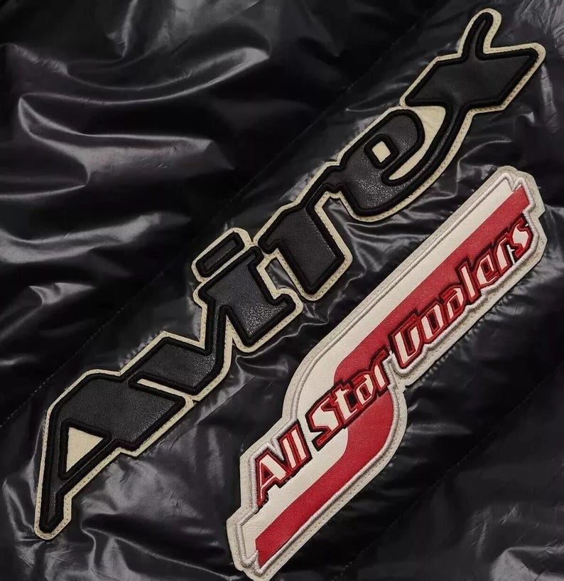 May include: Black jacket with two embroidered patches. One patch reads "AVIREX" in black letters with a cream border. The second patch says "All Star Coolers" in red and white.