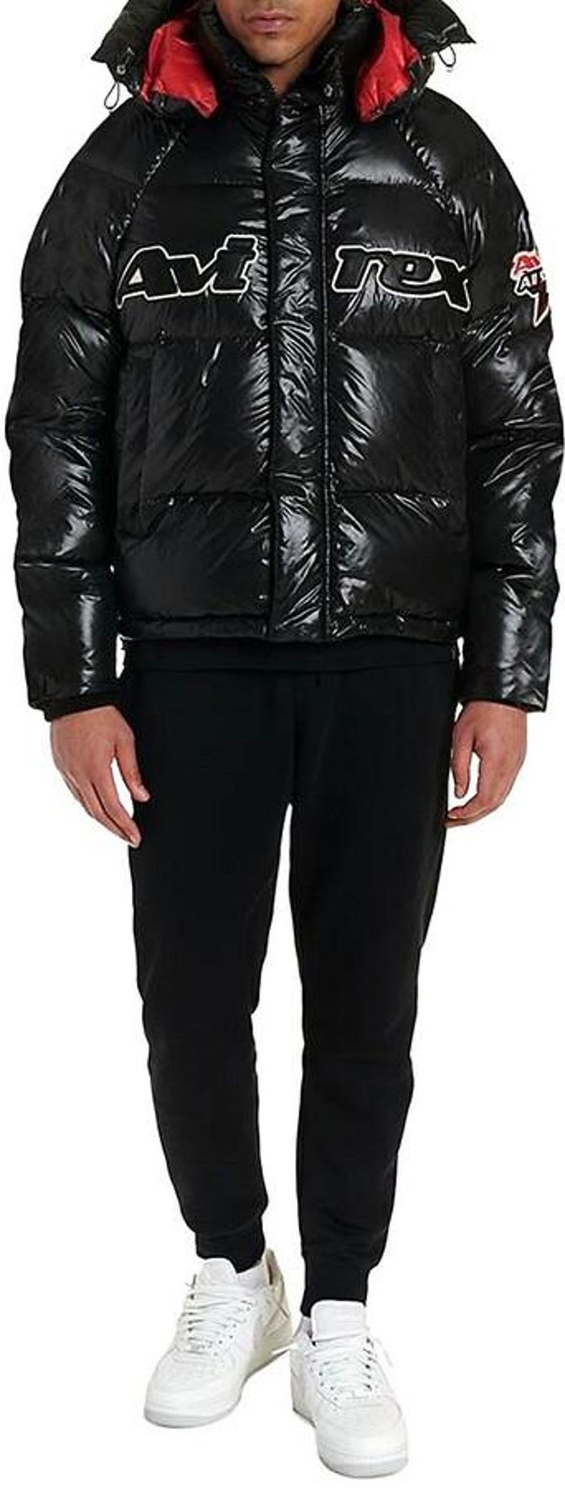 May include: Black puffer jacket with a hood and red lining. The jacket has the word "Avirex" in white lettering across the chest. The person is wearing black sweatpants and white sneakers.