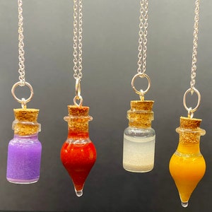 May include: Four glass bottle necklaces with cork stoppers and silver chains. The bottles are filled with different colored liquids: purple, orange, white, and yellow.