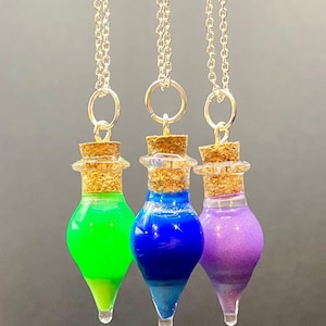 May include: Three glass bottle necklaces with cork stoppers. The bottles are filled with green, blue, and purple liquid. The necklaces are silver chains.