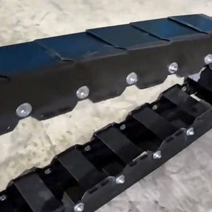 Peut inclure: Un assemblage de chenilles en métal noir avec plusieurs segments et des fixations argentées. La chenille est conçue pour une utilisation intensive, avec une construction robuste et une série de bandes de roulement connectées. L'image montre une partie de la chenille.