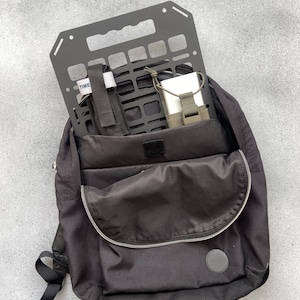 May include: A black backpack with a black metal grid organiser inside. The organiser has a white strap with the word "TIME" on it.