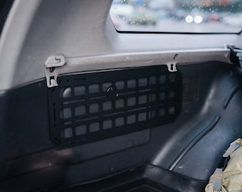 May include: A black metal cargo organizer with a grid pattern is mounted in the back of a car. The organizer is attached to the side panel of the car with two metal clips.