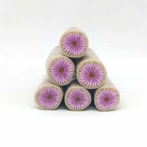 May include: Six beige polymer clay flower canes with pink and brown daisy designs. The canes are stacked in a pyramid shape.