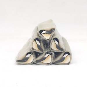 May include: A stack of six grey polymer clay canes with a black and white bird design. The canes are triangular in shape and are stacked in a pyramid formation.
