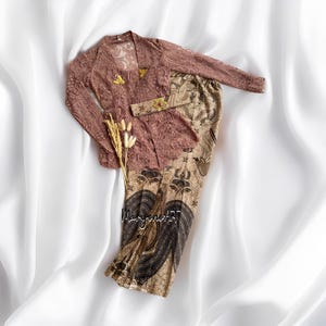 Könnte beinhalten: Ein zweiteiliges Outfit mit einem langärmeligen Spitzenoberteil mit einem floralen Muster in Brauntönen und einem passenden Rock mit einem floralen Druck in Brauntönen und Schwarz. Das Oberteil hat einen V-Ausschnitt und einen dekorativen Gürtel.