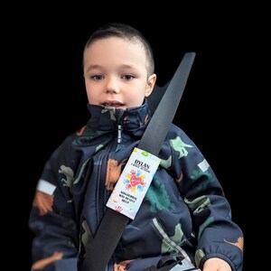 May include: A child wearing a navy blue dinosaur-patterned jacket with a seatbelt featuring a white label. The label reads "DYLAN I HAVE AUTISM" with a colorful heart and hand design, and the text "NON-VERBAL MAY RESIST HELP."