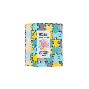 May include: A colorful, folded fabric item with a puzzle piece pattern in yellow, blue, gray, and cream. The item has a white label with the name "DYLAN", the text "I HAVE AUTISM", a heart with handprints, and the text "NON-VERBAL MAY RESIST HELP".