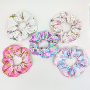 May include: Five colorful scrunchies with different unicorn and rainbow patterns. The scrunchies are made of soft fabric and are perfect for holding hair in place.