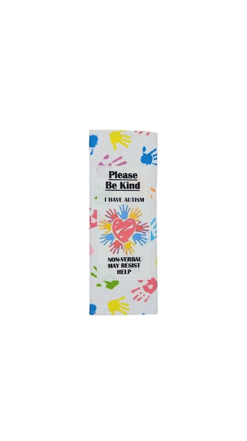 May include: White fabric item with colorful handprints and text. The text reads "Please Be Kind, I Have Autism, Non-Verbal May Resist Help". A heart is in the center of the design, surrounded by handprints.