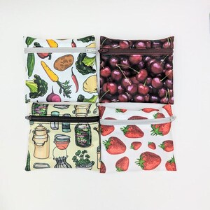 May include: Four small, square zippered pouches with different food-themed patterns. One features vegetables, another cherries, a third jars and containers, and the last strawberries. Each pouch has a contrasting zipper.