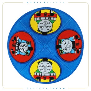 Może przedstawiać: Niebieska kippa z czterema żółtymi kółkami, z których każde przedstawia kreskówkową postać Thomasa the Tank Engine. Kippa jest wykonana z tkaniny i ma zszyty szew.