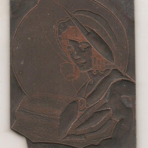 May include: A vintage relief print featuring a woman wearing a hat, with a circular backdrop. The print is primarily dark brown with reddish-brown details, showcasing the woman's face and hat. The woman is holding a fan.