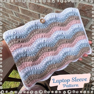 May include: A crocheted laptop sleeve in a wavy pattern, featuring pastel colors of pink, blue, and brown. The sleeve has a scalloped edge and a wooden button closure. The text "Laptop Sleeve Pattern" is visible.