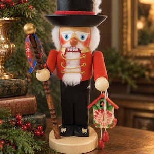 May include: A wooden nutcracker figure wearing a black top hat with a white feather, a red jacket with gold trim, and black trousers. It holds a brown staff with a patterned ribbon in one hand and a small cuckoo clock in the other hand.