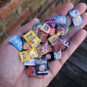 May include: A hand holding a variety of miniature snack chip bags. The bags are all different colors and feature various brand names, including Lay's, Fritos, and Doritos.