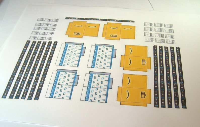 Peut inclure: Une feuille de papier imprimable avec des instructions et des mod&egrave;les pour construire une bo&icirc;te en carton. La bo&icirc;te est jaune avec un logo Amazon brun et le texte "Amazon" imprim&eacute; dessus. La feuille comprend &eacute;galement des mod&egrave;les pour les rabats de la bo&icirc;te et un motif de carr&eacute;s bleus et blancs.