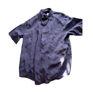 以下が含まれることがあります： 濃い青色のボタンダウンの半袖シャツ。シャツの左胸にポケットが1つ付いている。